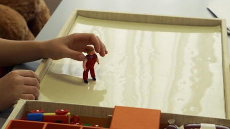 Eine Kinderhände stellt eine Spielfigur auf einen Tisch, Filmstill aus "Wie die anderen"